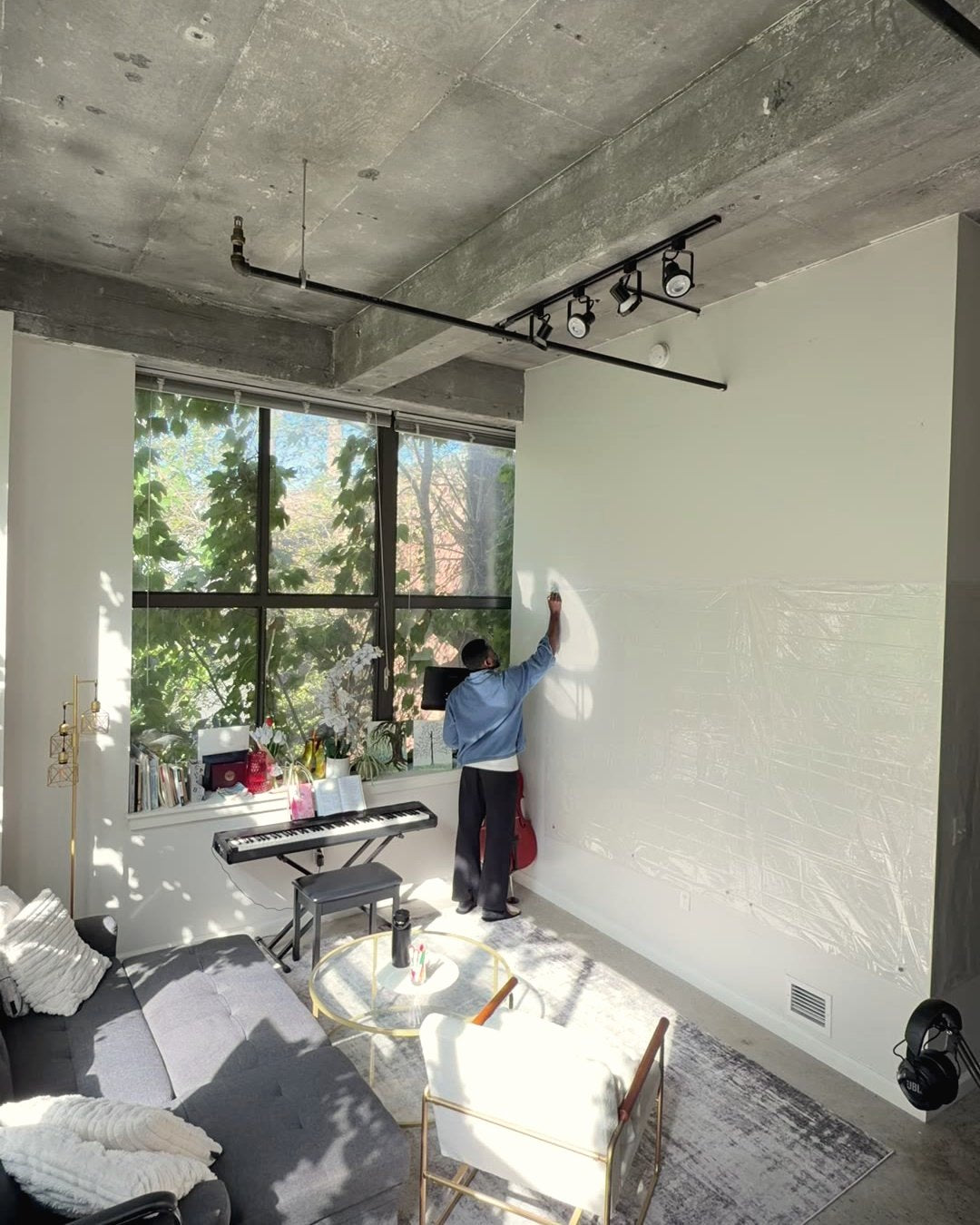 A student pressing a blank clear sheet onto a white wall beside a sunlit window.